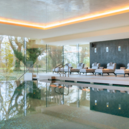 Luxurious indoor swimming pool with elegant arched windows, surrounded by comfortable lounge chairs, set within the opulent Adare Manor with serene lighting and a tranquil atmosphere.