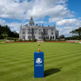 Elegant room in Adare Manor featuring a cozy fireplace, luxurious seating, ornate ceiling, and large windows showcasing lush garden views. Classic opulent decor creates a warm, inviting atmosphere.