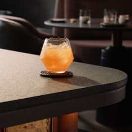 Elegant cocktail with a frothy top, garnished with a lemon twist, served in a stylish glass at Oku Restaurant, Adare Manor. Plush dining setting in the background.