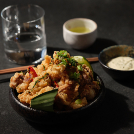 A gourmet dish featuring exquisitely plated seafood garnished with microgreens, showcasing culinary artistry with vibrant colors and elegant presentation on a white oval plate against a dark background.