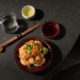 A gourmet dish presented artistically on a white plate, featuring sliced cooked meat, garnished with sauce, fresh herbs, and finely chopped vegetables, served at a high-end restaurant.