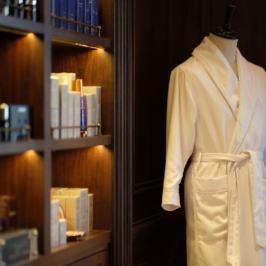 Elegant, luxurious boutique showcasing high-end women's designer clothing, accessories, and a large mirror. The room is softly lit, highlighting the sophisticated interior design and curated fashion display.