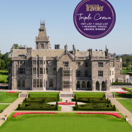 A luxurious garden with meticulously manicured lawns, blooming flowers, and elegant statues, nestled alongside a grand manor in the background under a clear blue sky.