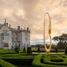 Guests stroll manicured gardens before Adare Manor's Gothic Revival façade and golden sculpture at sunset, Adare, County Limerick, Ireland